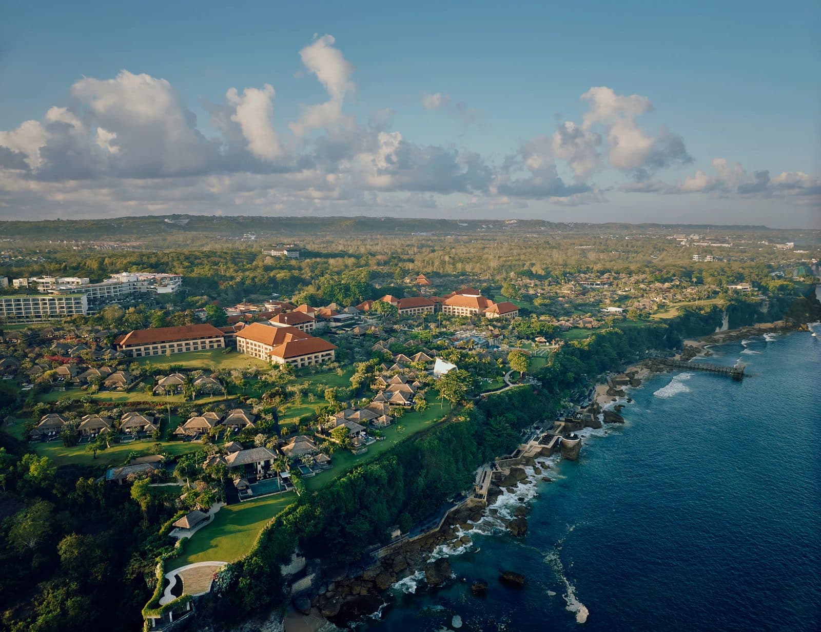 AYANA Bali from above: orange-roofed buildings and villas in gardens on a cliff edge above the ocean