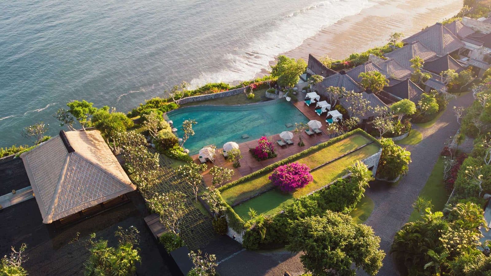 Aerial view of Bvlgari Resort Bali at sunset: the main pool and lawns on the cliff edge, with beach and ocean below