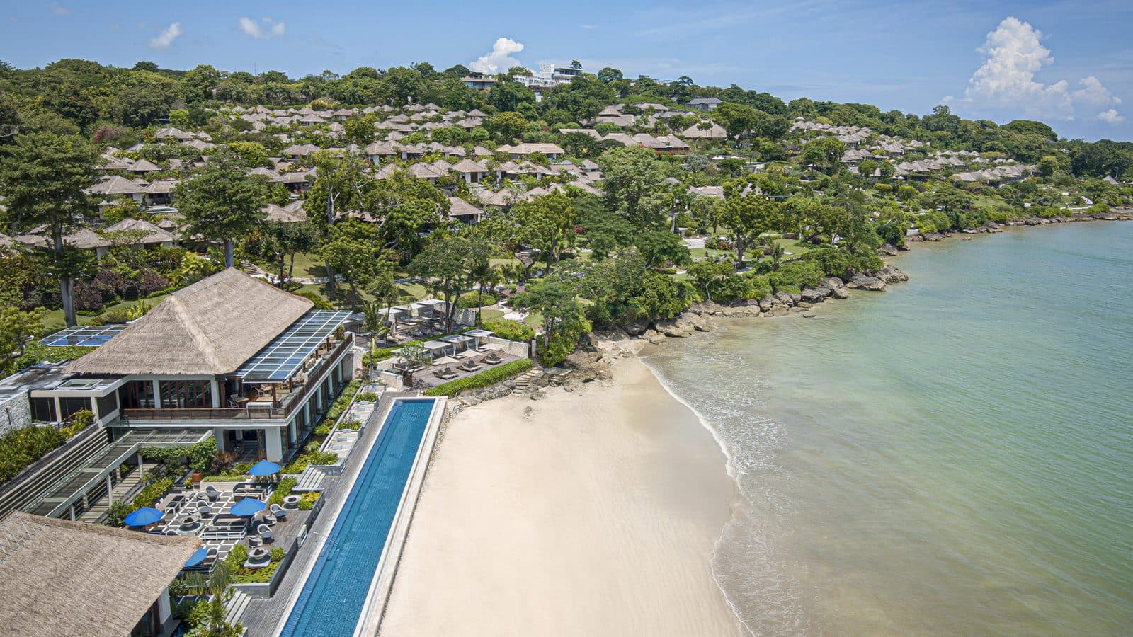 Aerial view of Four Seasons Jimbaran Bay: thatched villas on the slope, the long Sundara pool beside the beach and the bay