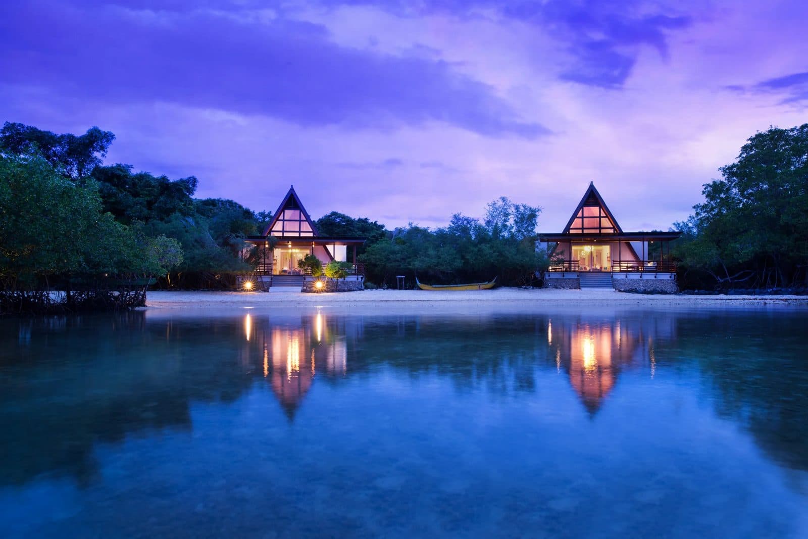 Two Ocean Front Mangrove villas with triangular roofs at dusk: lit windows reflected in calm water, surrounded by mangroves