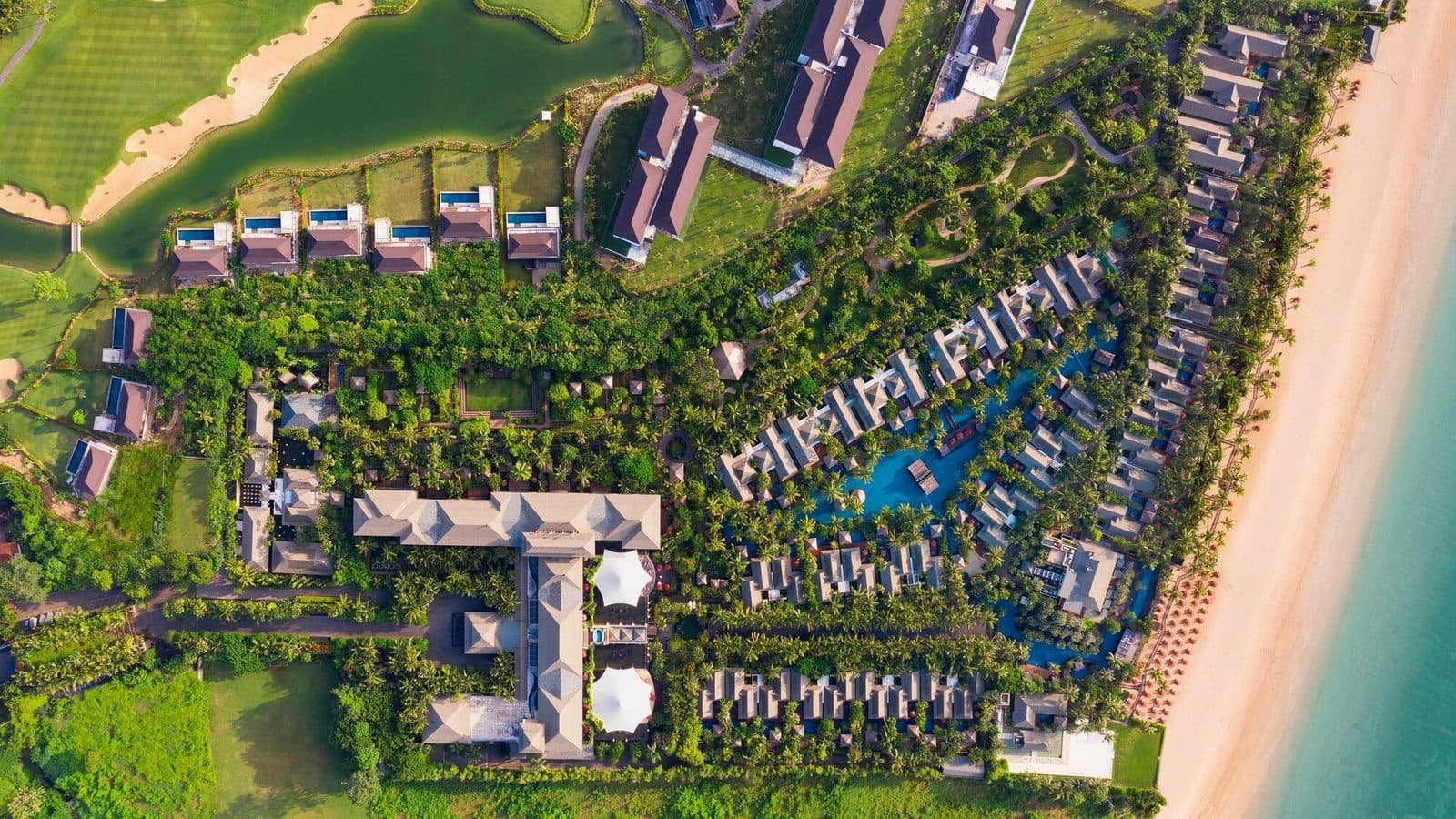 Aerial view of The St. Regis Bali Resort: the main building, villas around a blue lagoon, a beachfront along the ocean and a golf course with a pond