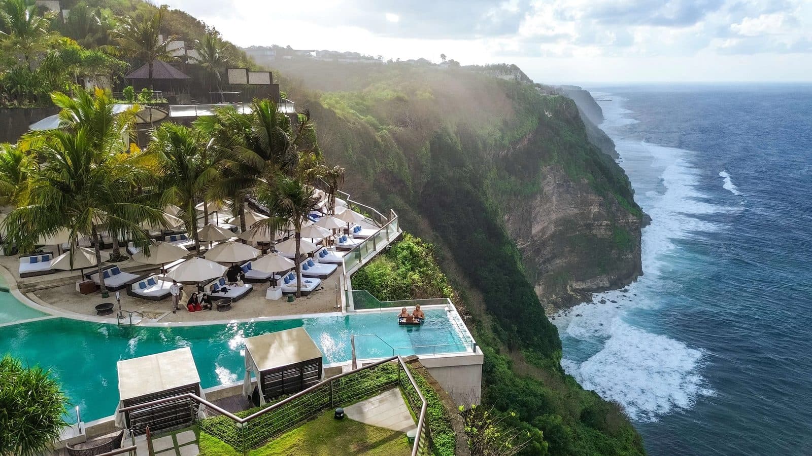 oneeighty° club on Uluwatu's cliffs: loungers under umbrellas, a glass-bottomed pool above the drop and ocean surf below