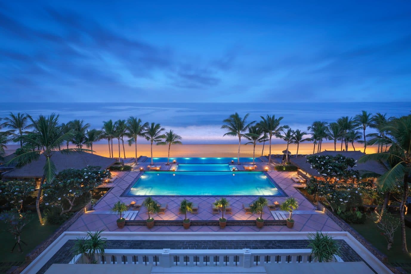 The Legian's stepped infinity pool at dusk: illuminated water, palms and sunset above Seminyak Beach
