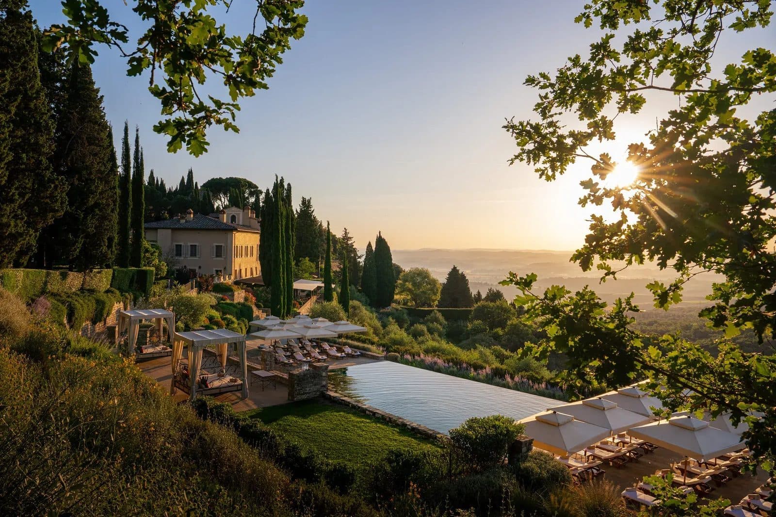 A pool and stone borgo buildings among cypresses in sunrise light