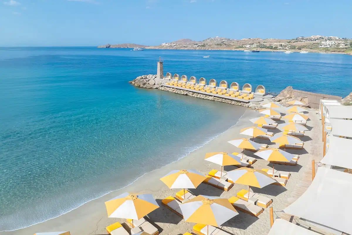 Santa Marina beach with yellow umbrellas and a breakwater in Ornos Bay