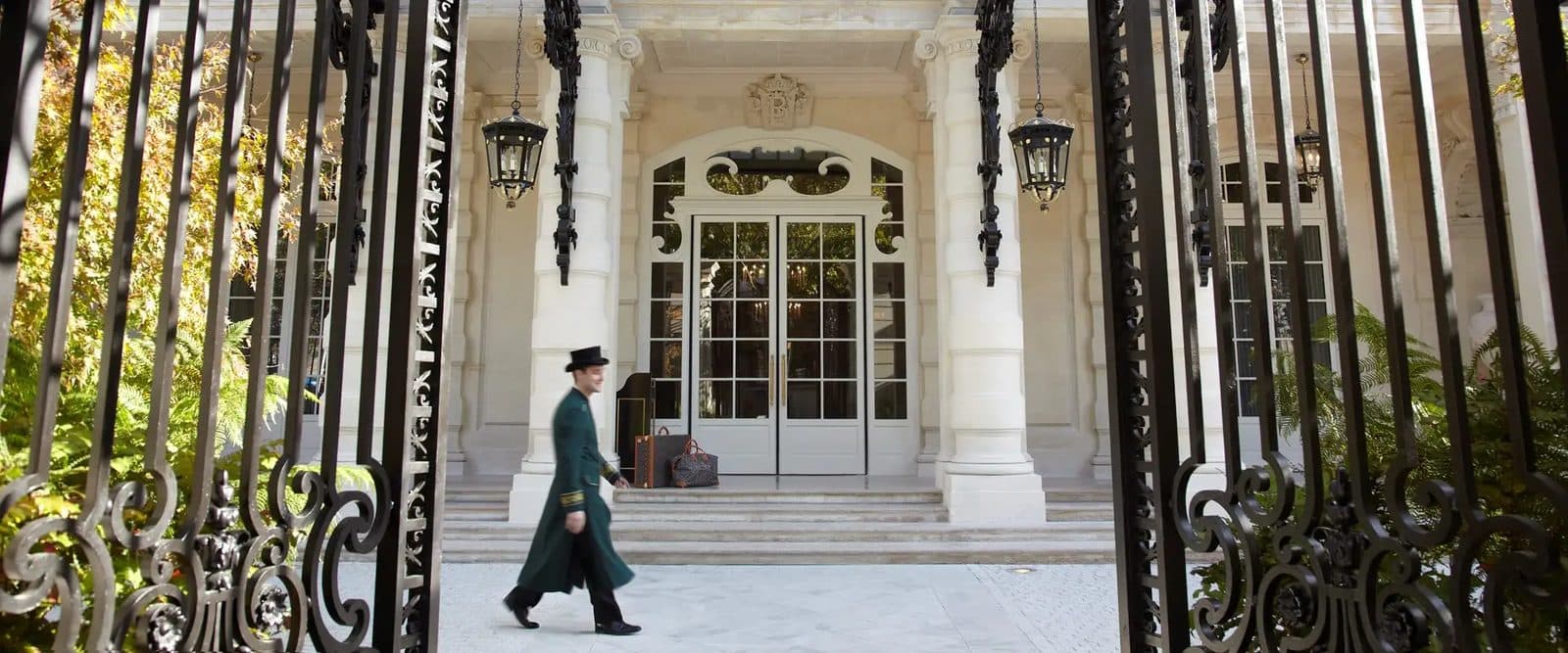 The entrance to Shangri-La Paris behind wrought-iron gates, with a hotel employee walking by the stairs