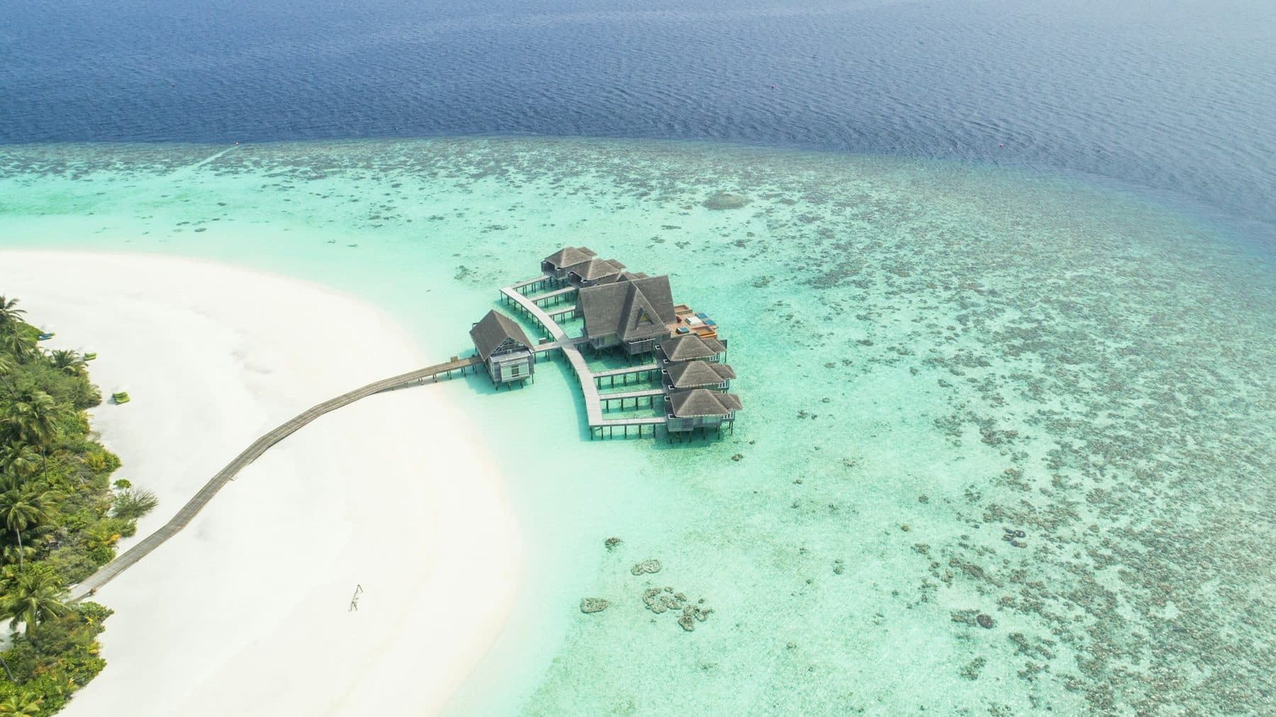 A spa on stilts above the reef, reached by walkways from a white beach, viewed from the air