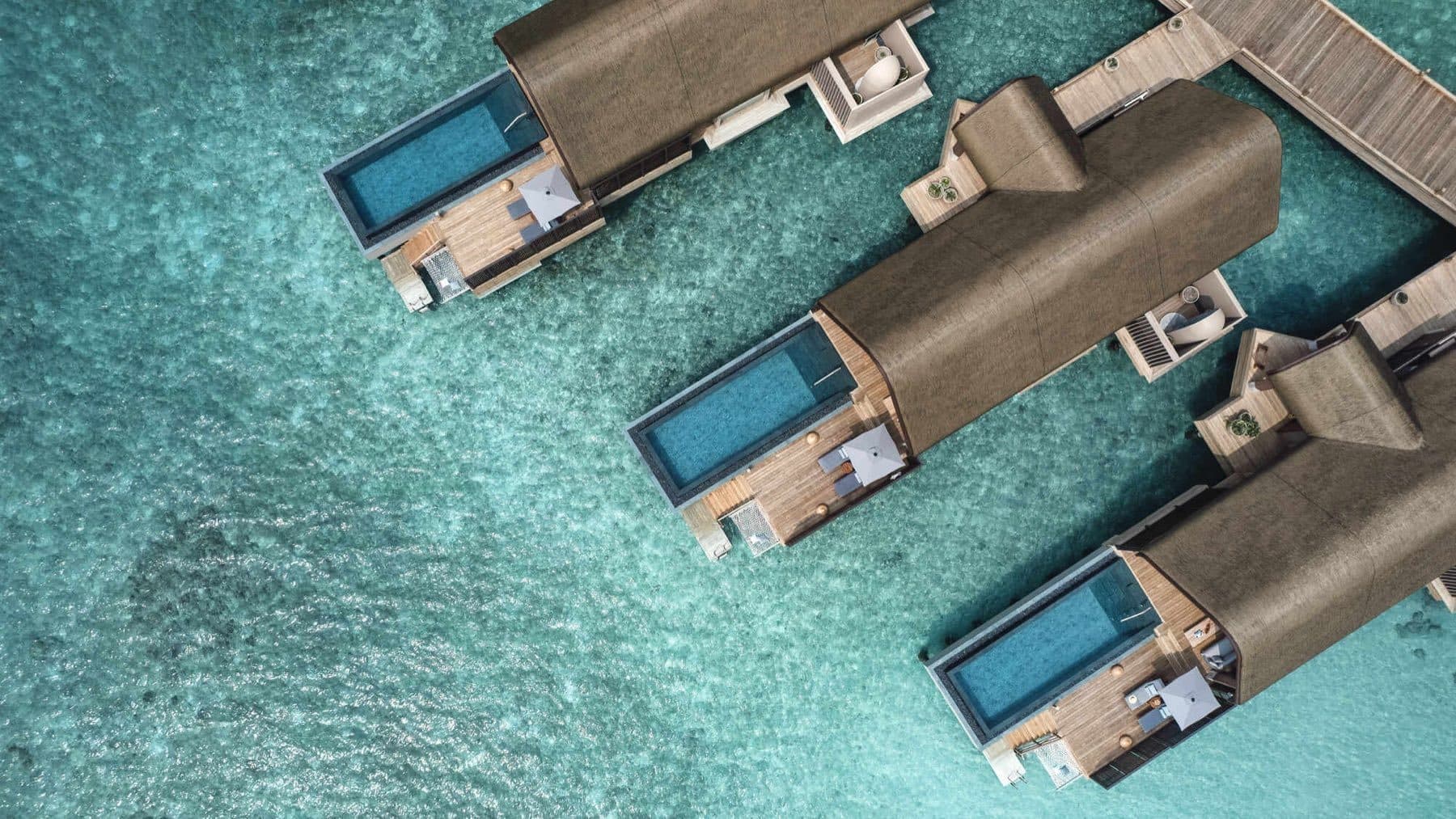Aerial view of three overwater villas with rectangular pools and terraces above a turquoise lagoon