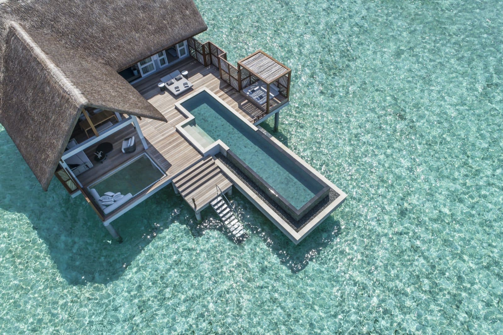 Aerial view of a thatched overwater villa with a long pool and steps into the lagoon