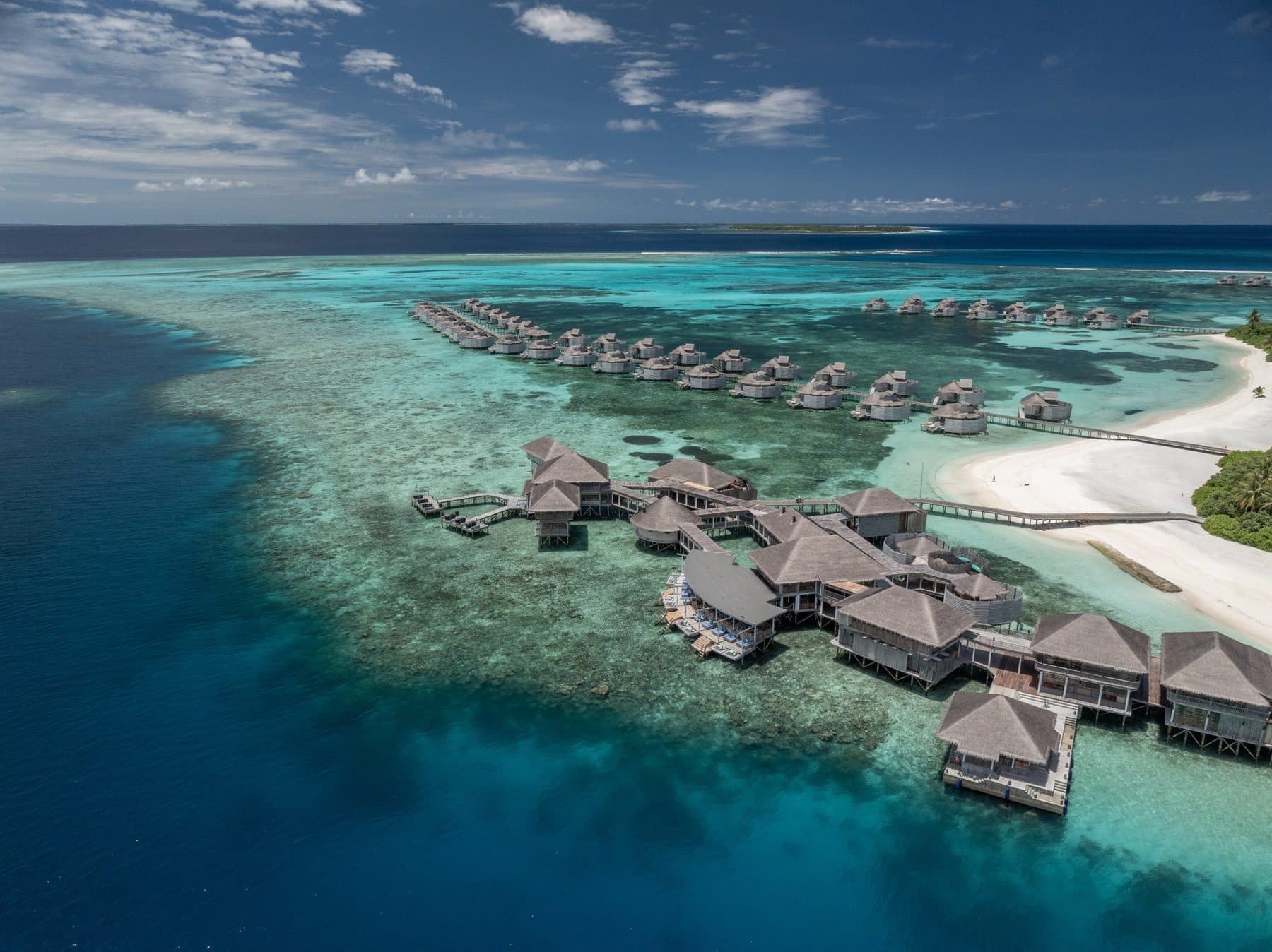 Stilt villas along the edge of the reef and the island's white beach, viewed from the air