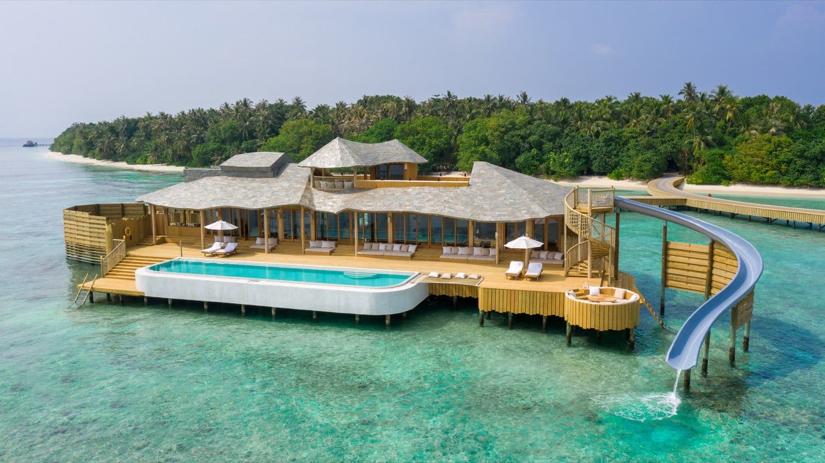 A villa above the lagoon with a long pool, terrace and waterslide into the sea, with the island's palm-lined shore behind it