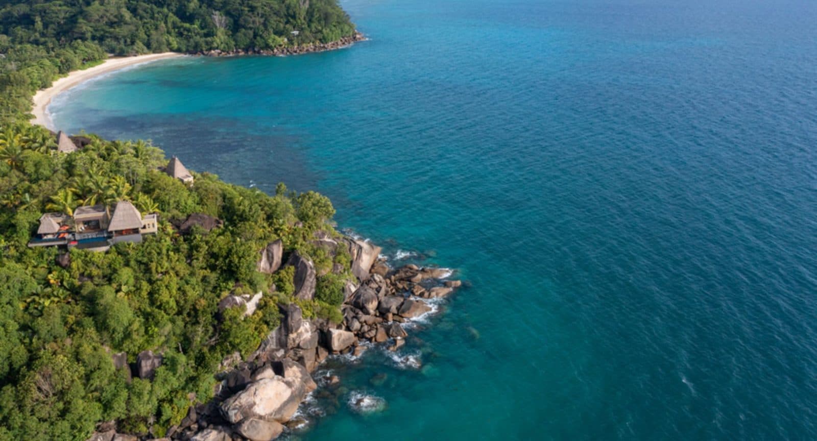 Aerial view of the Anantara Maia peninsula: thatched villas on a rocky headland, turquoise water and a beach in the distance