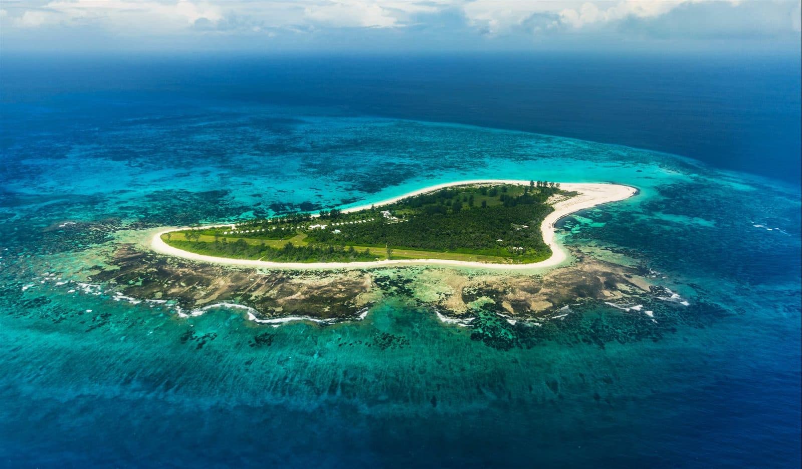 Aerial view of Bird Island: a flat green island inside a ring of white beach, surrounded by a coral reef and turquoise water