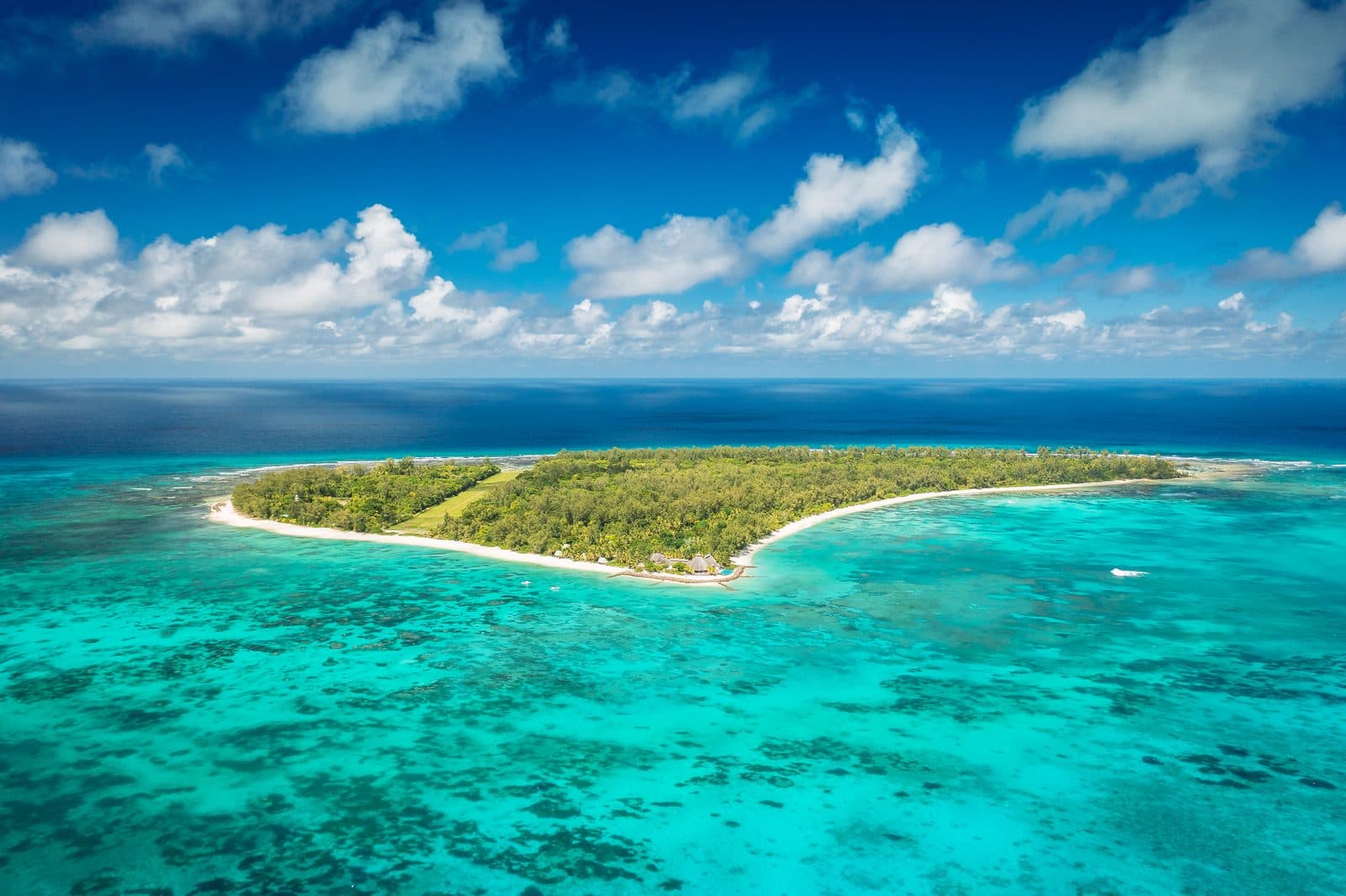 Aerial view of Denis Island: forest inside a ring of white beach, surrounded by a turquoise lagoon with reefs and the deep blue ocean