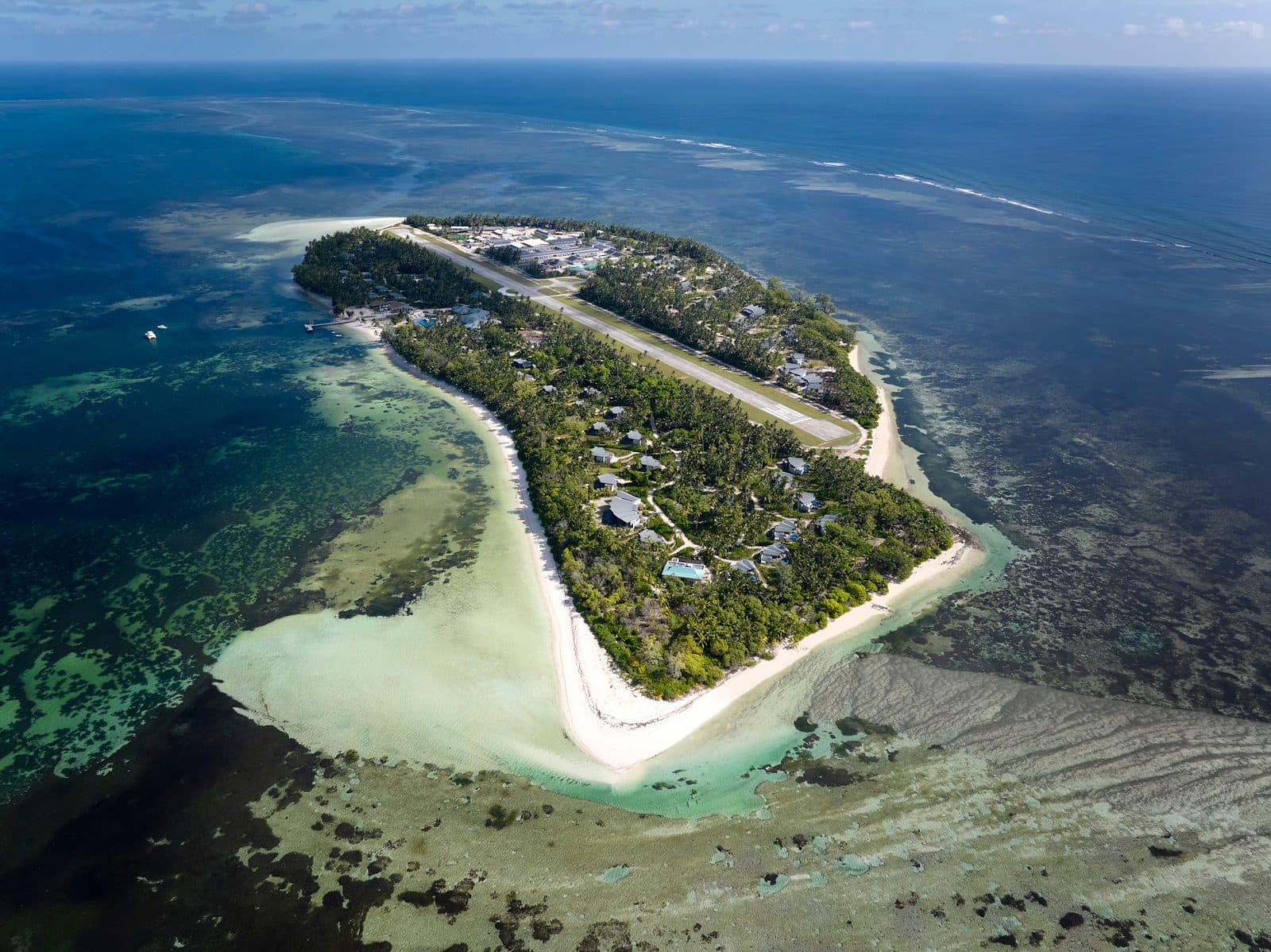 Aerial view of Platte Island: a narrow strip of land with an airstrip, villas among palms, a white sand spit and surrounding reefs