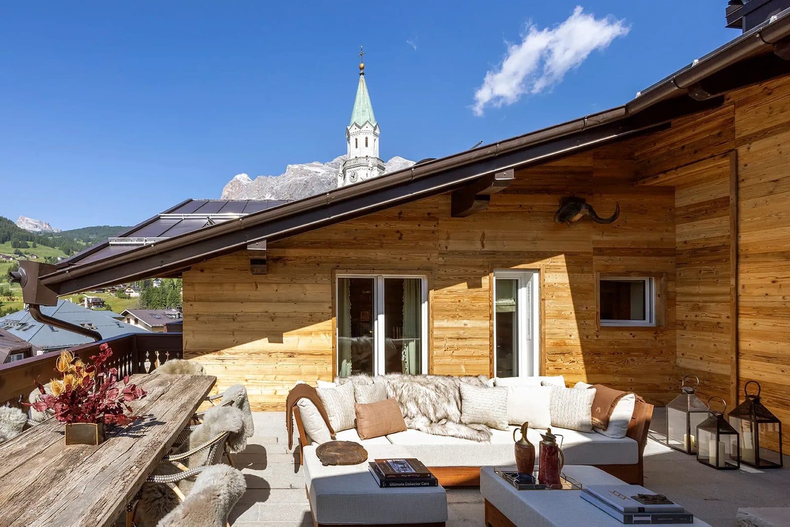 A terrace with wooden walls, sofas and flowers beneath Cortina’s bell tower