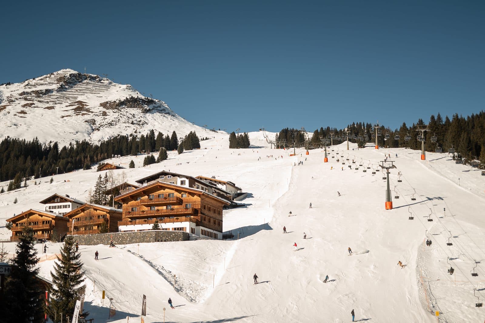 Wooden Aurelio buildings beside a snowy piste and chairlift