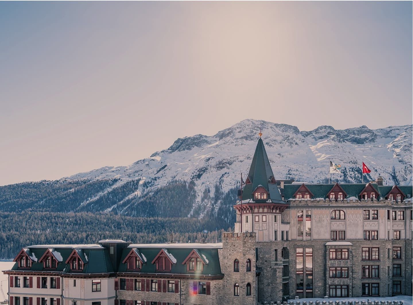 The tower and façade of Badrutt’s Palace before snowy mountains in morning light
