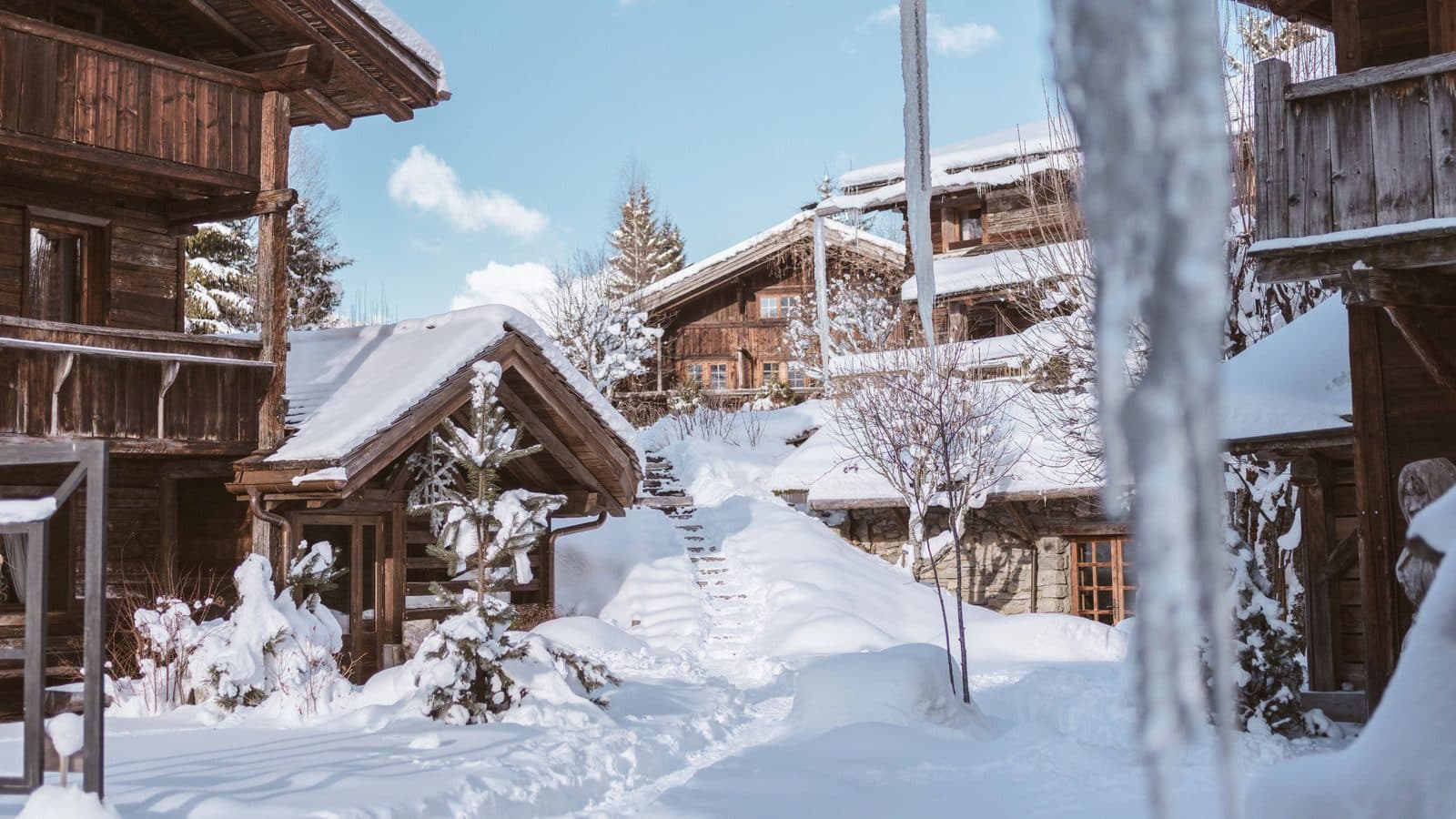 Wooden Les Fermes de Marie chalets among snowdrifts, snowy branches and a passage between the buildings