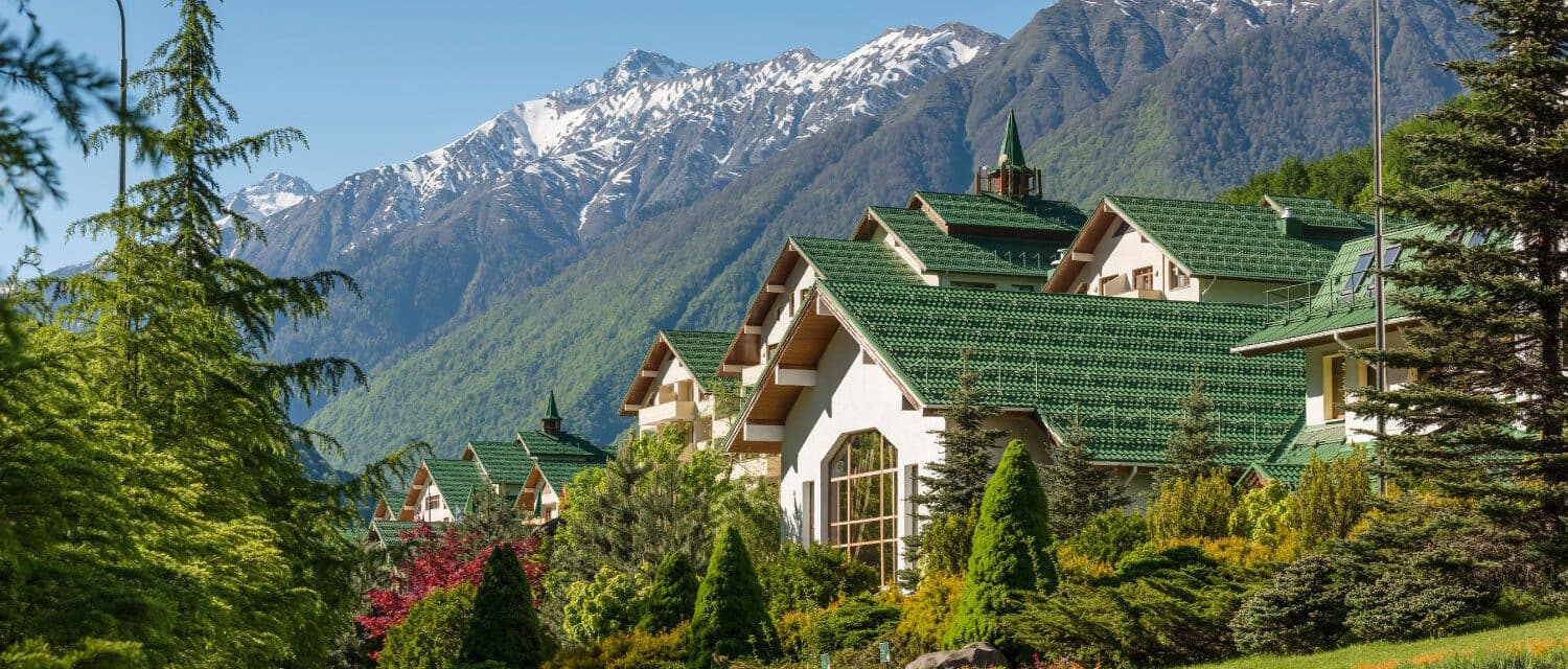 Hotel buildings with green roofs among trees against snowy mountains