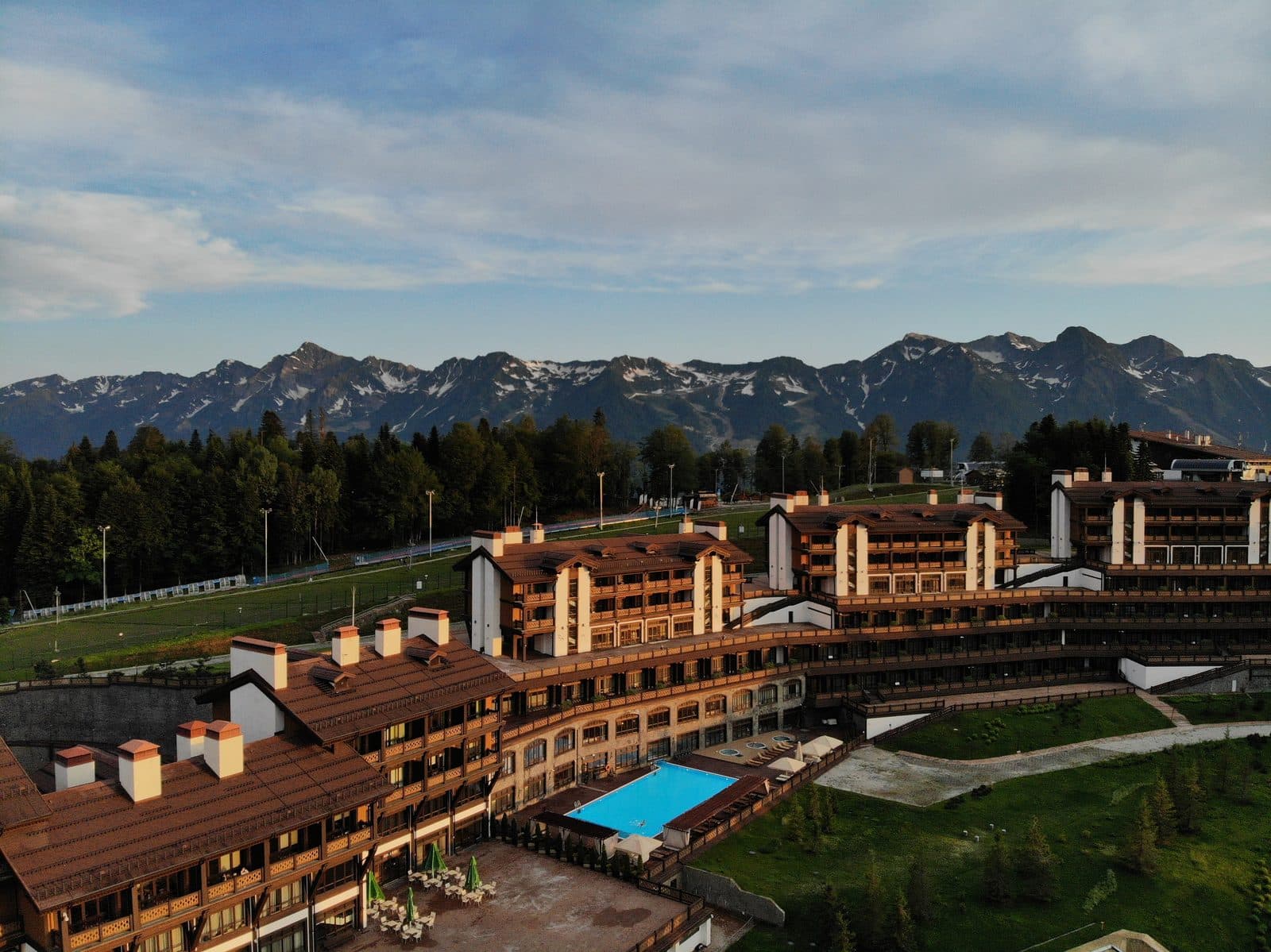 A hotel with wooden façades and an outdoor pool against a mountain ridge