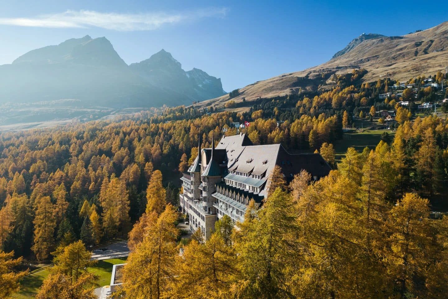 Aerial view of Suvretta House among golden larches on a mountainside in autumn