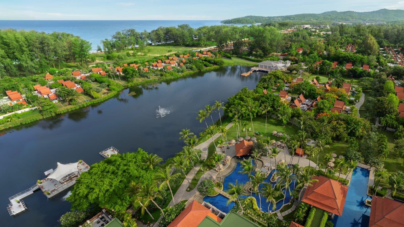 Aerial view of Banyan Tree Phuket: a lagoon with a floating pavilion, pools among palms, orange villa roofs and sea on the horizon