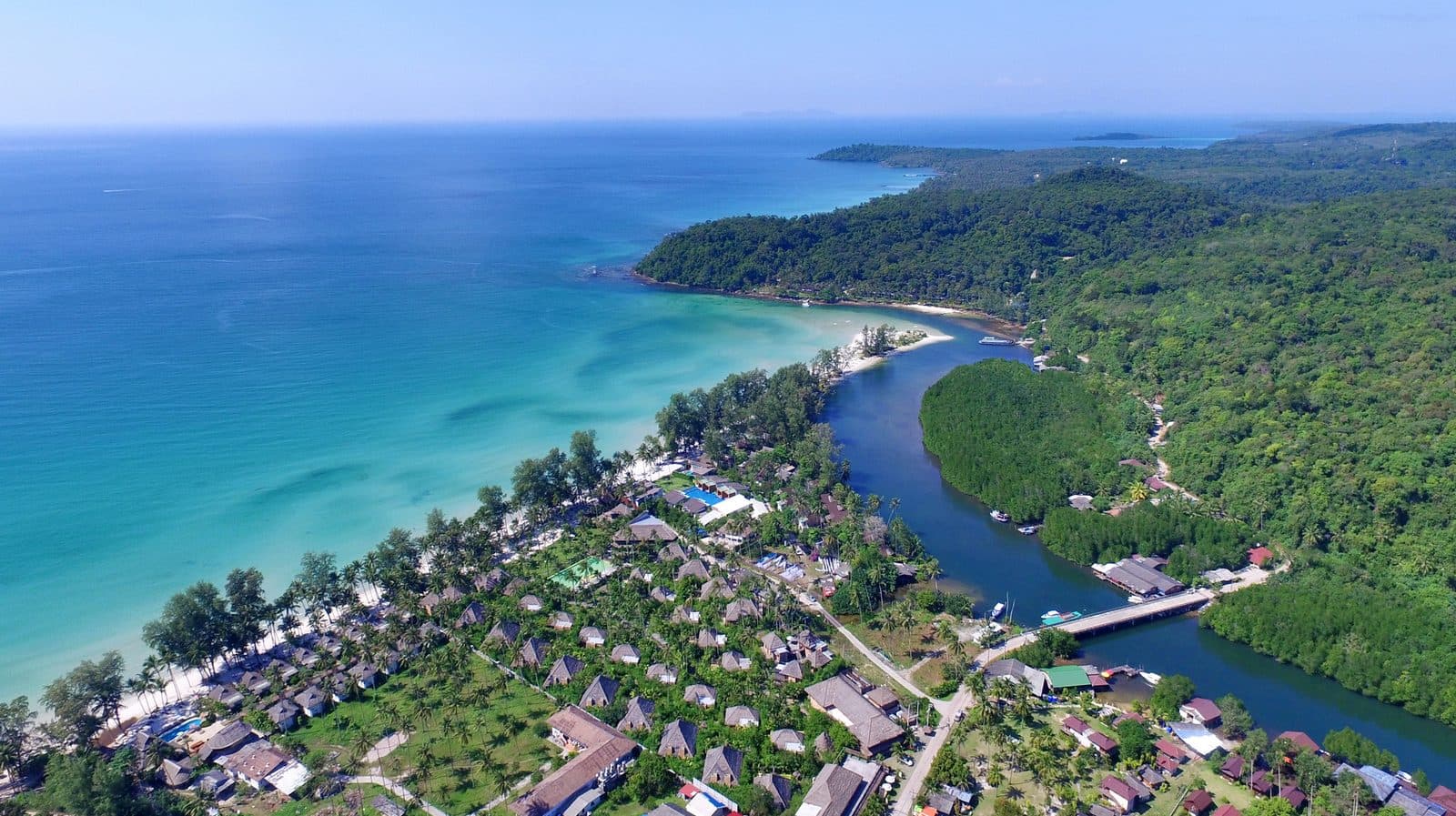 Aerial view of Klong Chao Beach: a strip of white sand, turquoise sea, a river mouth in mangroves and villa roofs among palms