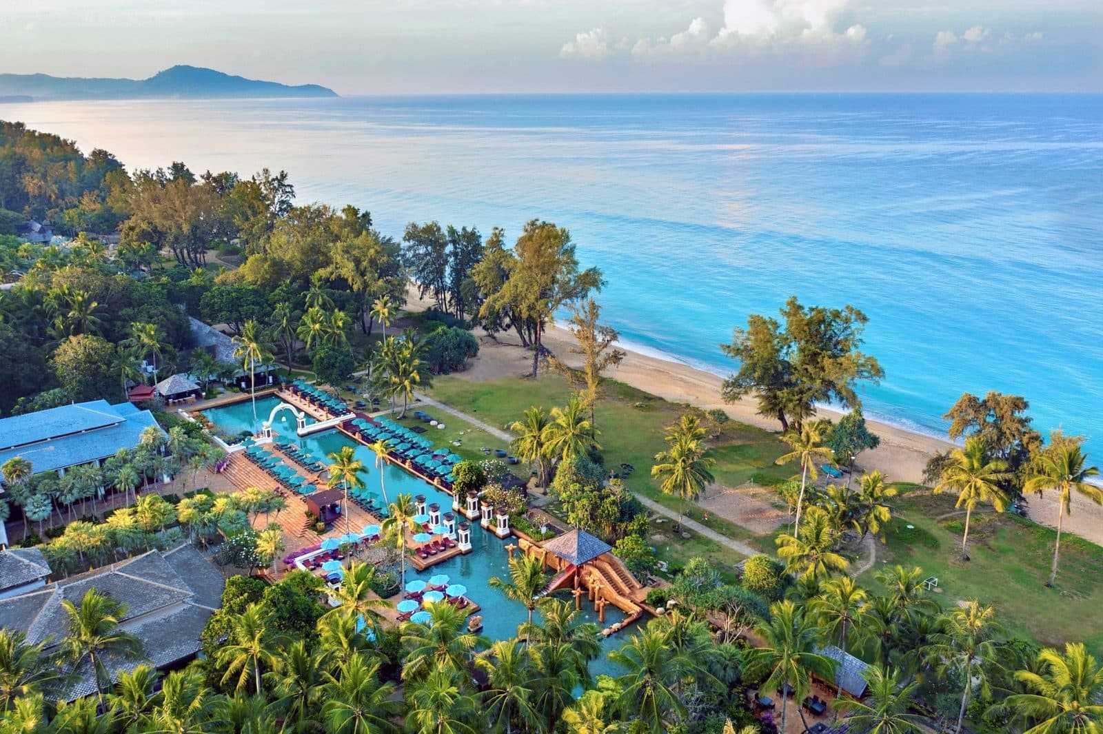 Aerial view of JW Marriott Phuket: lagoon pools among palms, lawn and the long Mai Khao Beach beside turquoise sea