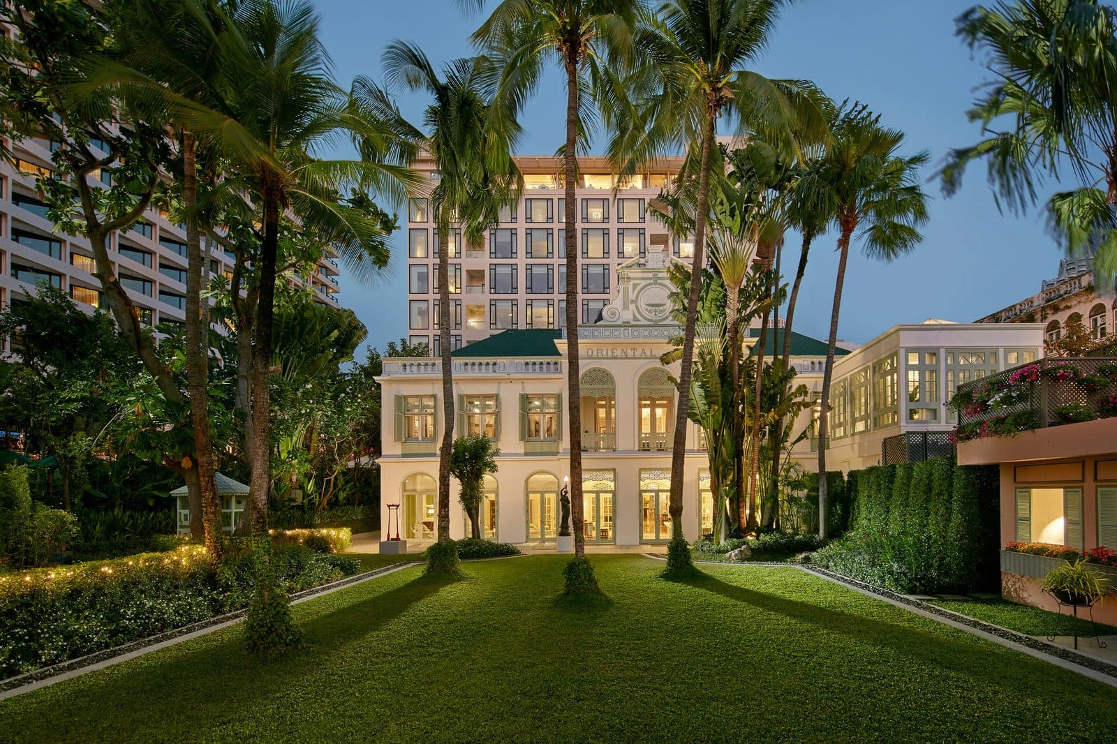 Historic Authors' Wing at dusk: a white façade with a green roof, tall palms and lawn, with a high-rise hotel building behind