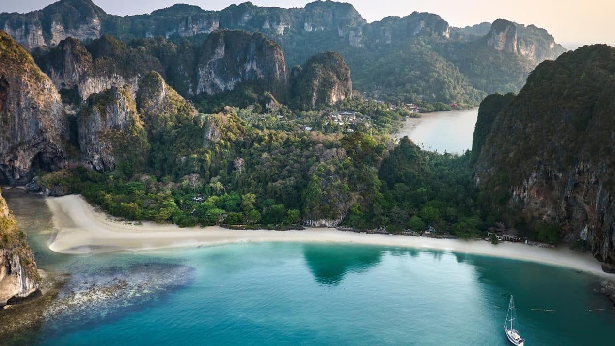 Aerial view of Railay Peninsula: limestone cliffs in the jungle, a white beach and a turquoise bay with a yacht