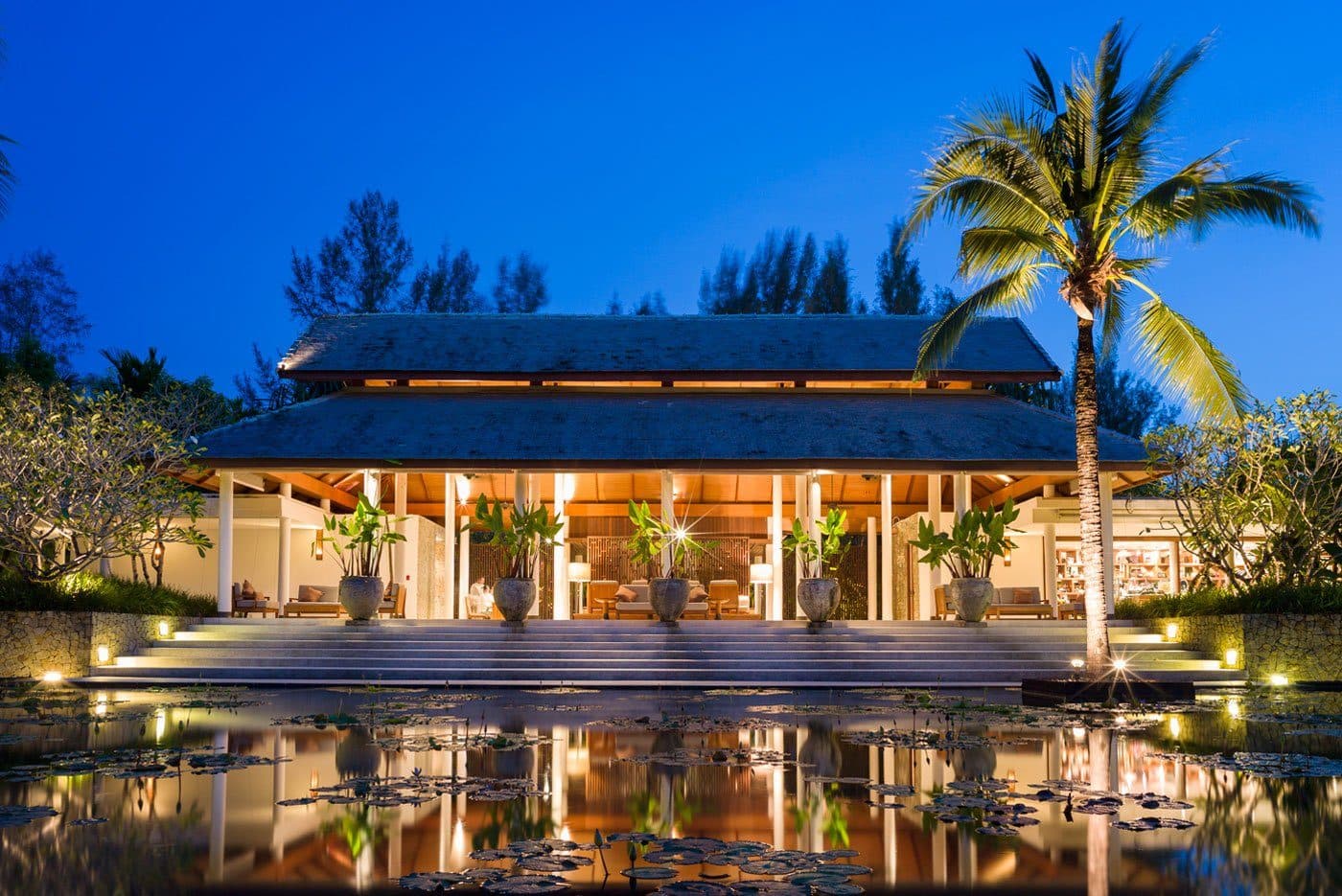 The Sarojin's main pavilion at dusk: a two-tier Thai roof, steps to a water-lily pond and an illuminated palm