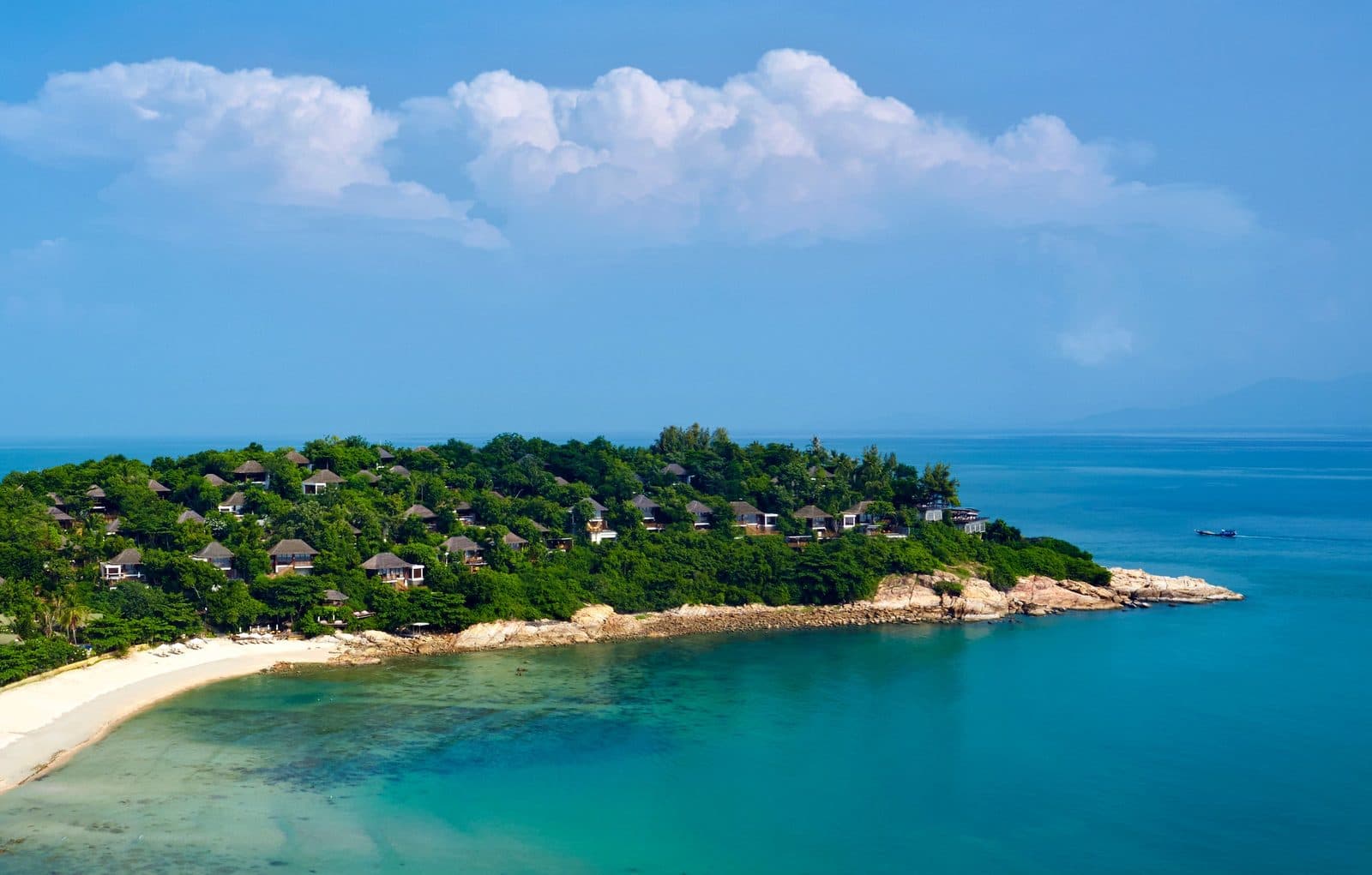 Six Senses Samui headland: dark-roofed villas among trees, a rocky shore, a strip of beach and a turquoise bay