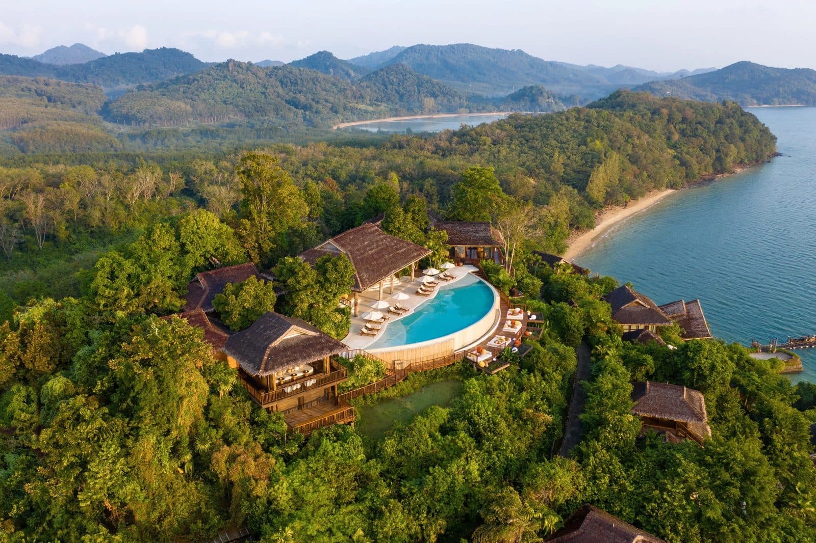 Aerial view of The Hilltop, the resort's highest point: a circular infinity pool, Thai roofs among jungle and Koh Yao Noi's shore