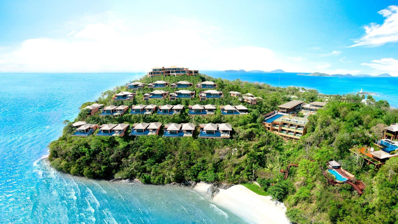 Aerial view of Cape Panwa: villas terraced on a green slope, buildings with pools on the right, a white-beach bay and turquoise water