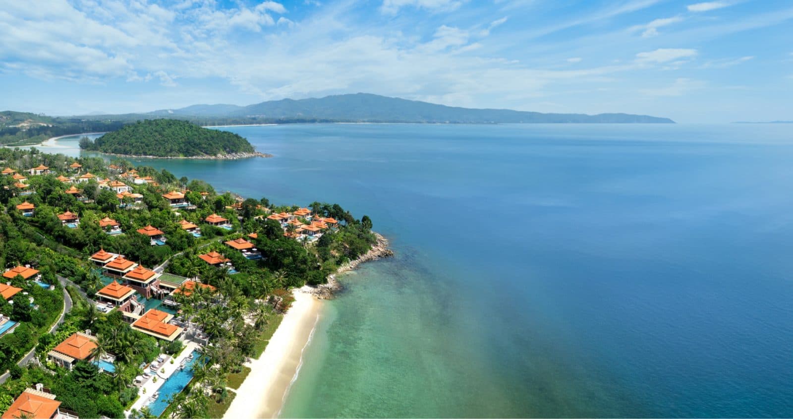 Aerial view of Trisara: orange-roofed villas on a green slope, a beachfront pool, pale sand and turquoise sea with an island