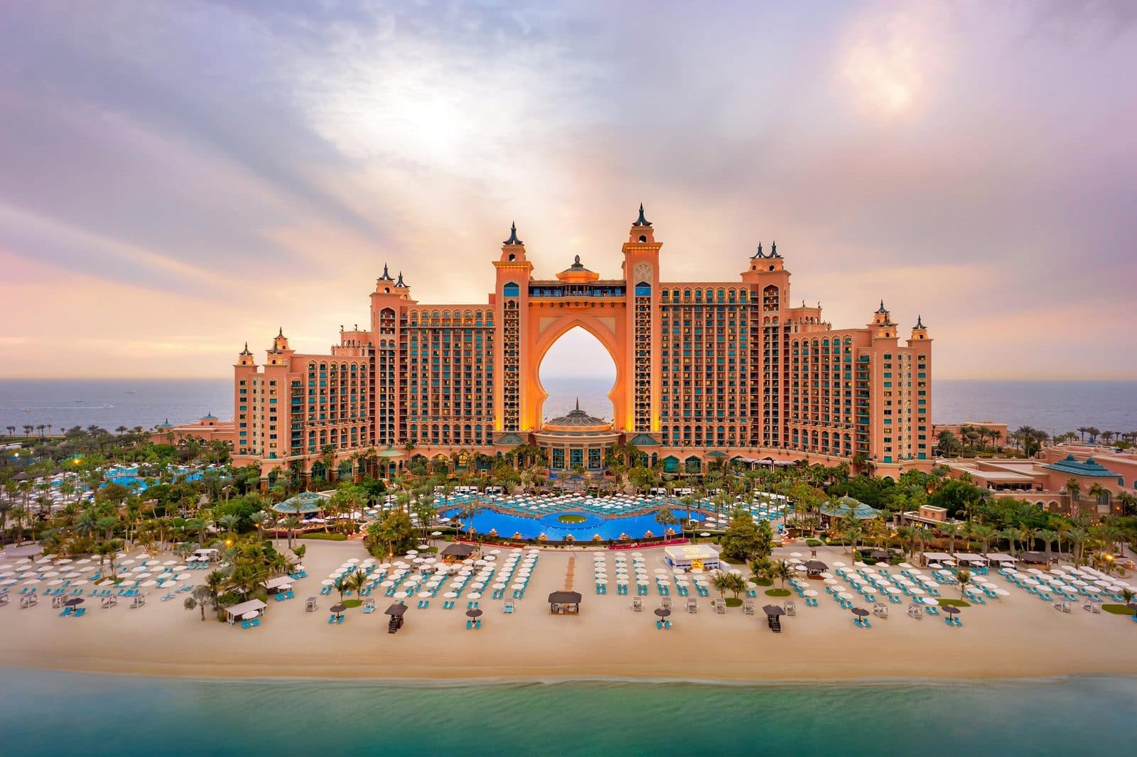 Atlantis, The Palm at sunset: pink towers with a huge central arch, palm-fringed pools and rows of beach loungers beside the sea