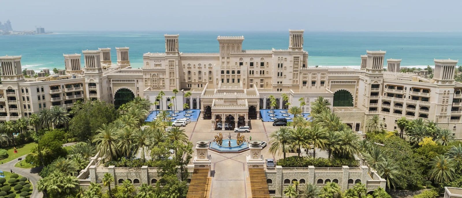 Aerial view of Jumeirah Al Qasr: a palace with windcatcher towers, a ceremonial courtyard with fountains and palms, and the Gulf beyond
