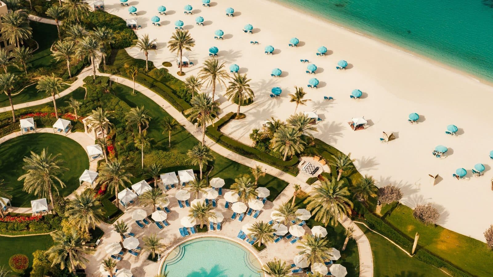 Aerial view of One&Only Royal Mirage: a beach with turquoise umbrellas, palm gardens with winding paths and a round pool