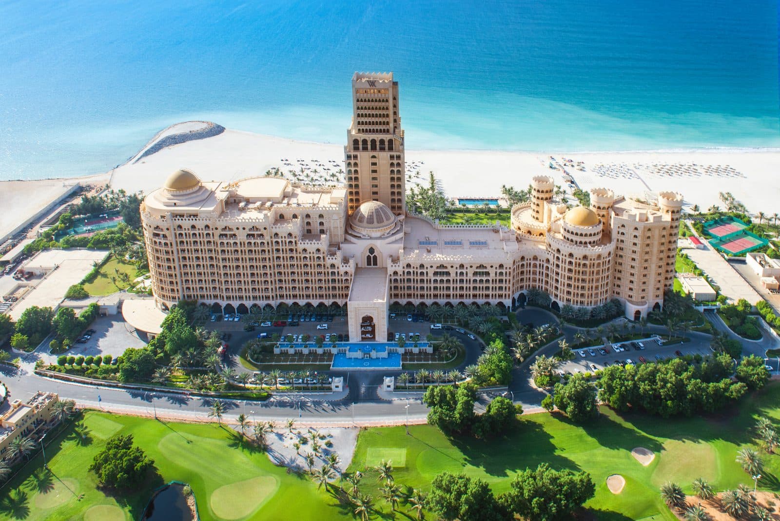 Aerial view of Waldorf Astoria Ras Al Khaimah: a building with domes and a tower, white beach and Gulf behind, and golf course in the foreground
