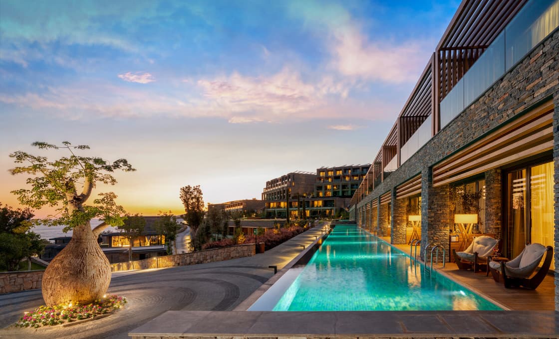 A poolside terrace and resort buildings in Bodrum at sunset.
