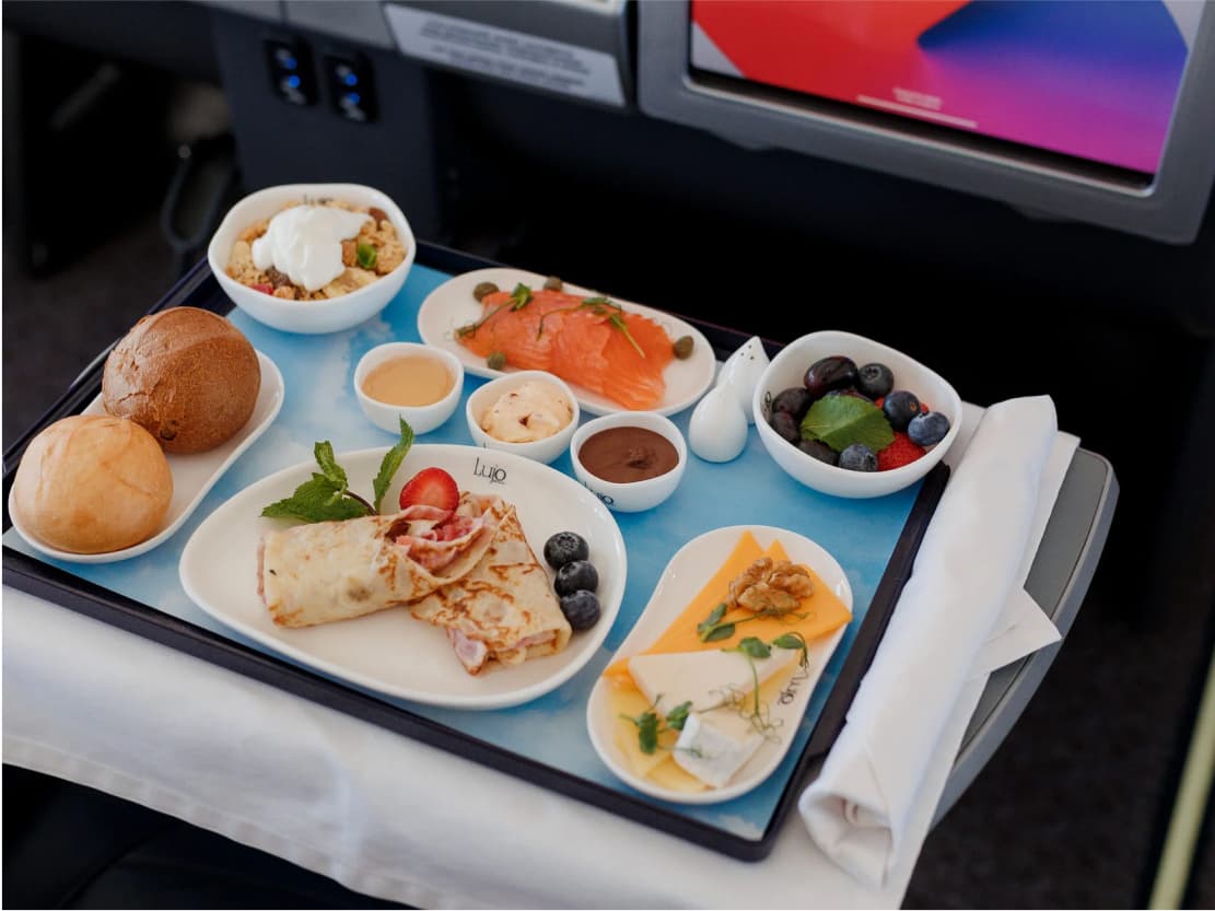 A meal setting on a table beside a Lujo BlackJet seat: several dishes and an individual screen.